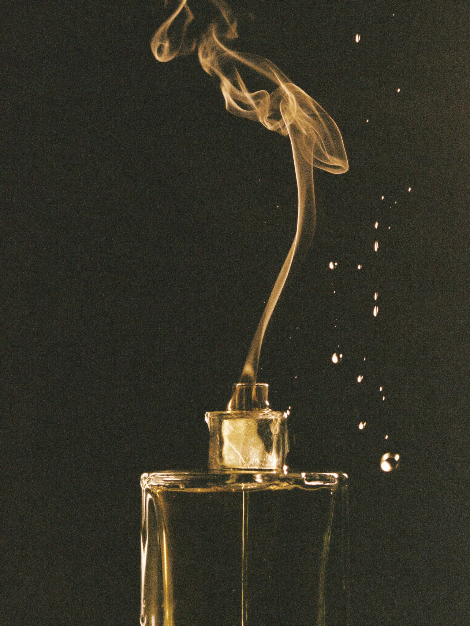 Macro of liquid perfume catching light — champagne and platinum.